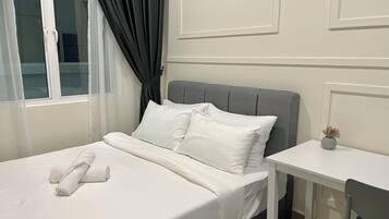 Uma cama bem arrumada com lençóis e almofadas brancas, um painel de cabeceira estofado em cinza, uma pequena mesa de cabeceira com um vaso, e uma janela com cortinas brancas.