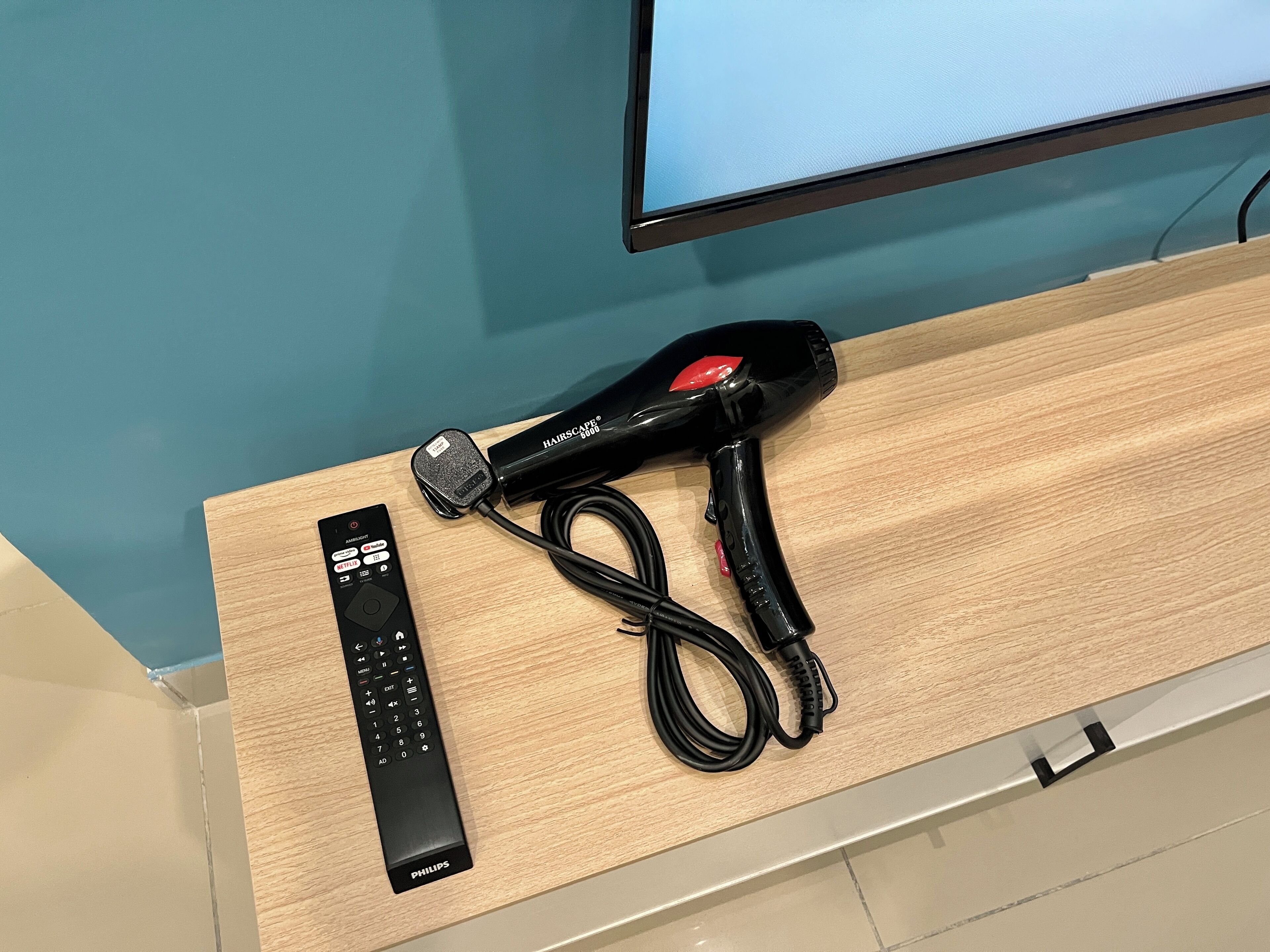 A Philips remote control and a black hairdryer on a wooden surface.