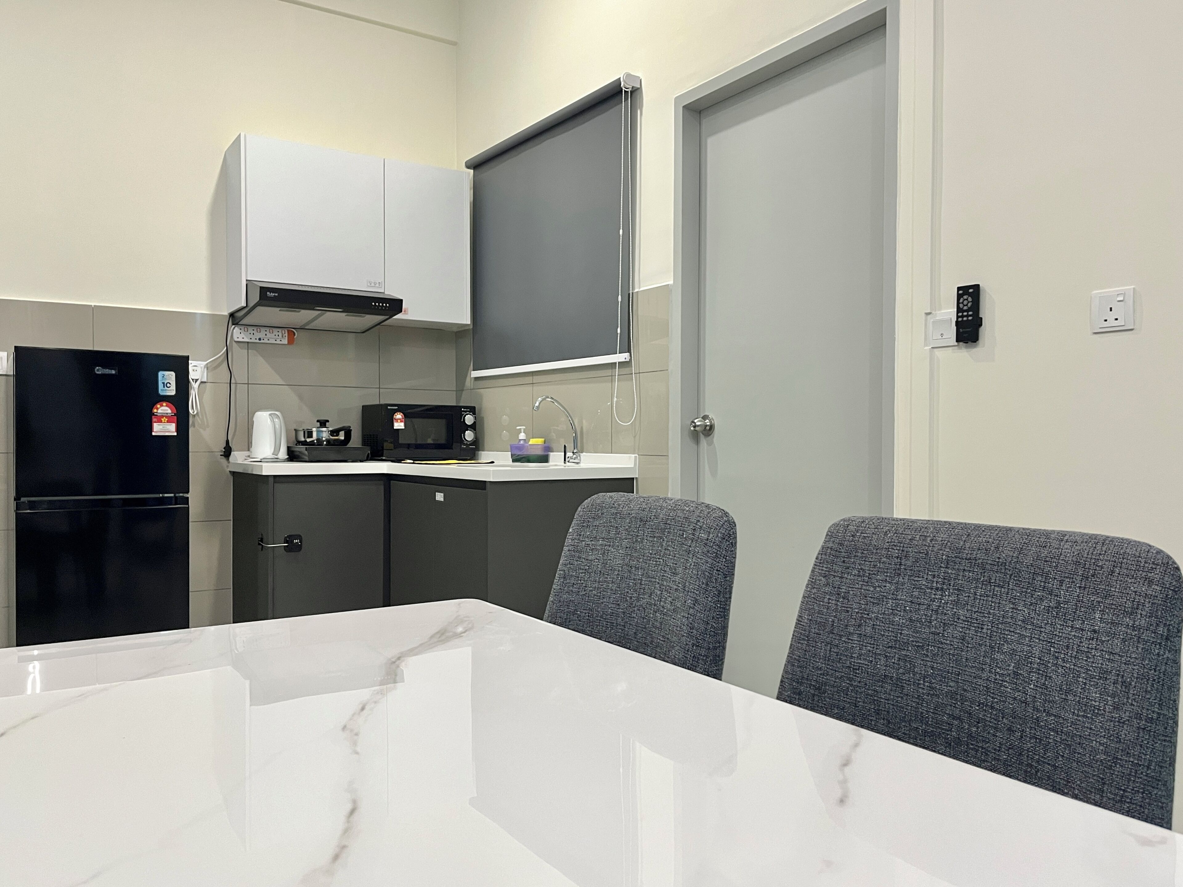 A compact kitchen with a refrigerator, microwave, and sink. There is a white marble table with two grey chairs.