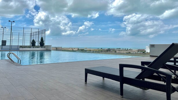 Ein Poolbereich mit Liegestühlen, einem Pool und Blick auf Strand und Gebäude in der Ferne.