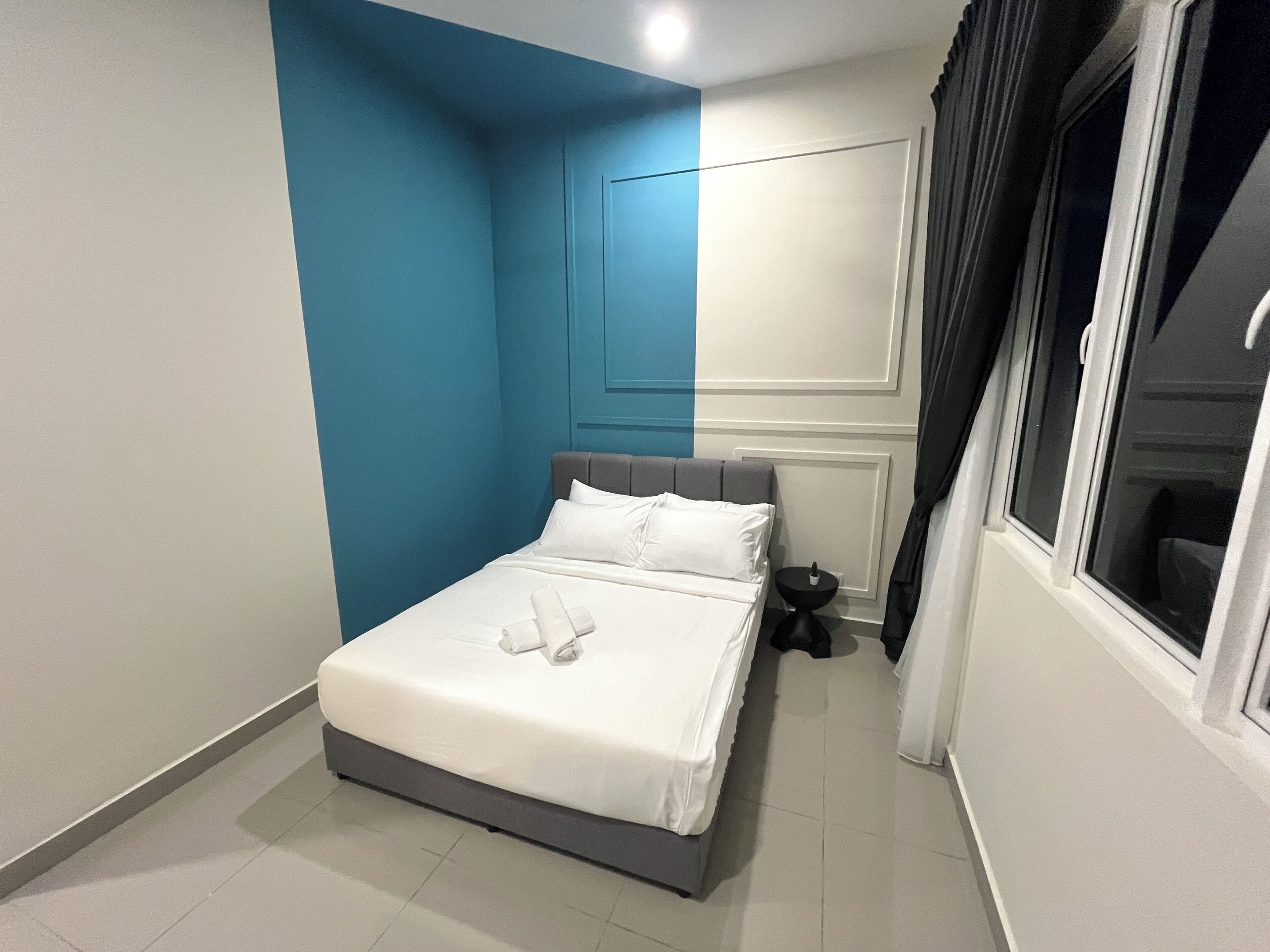 A neatly made bed with white linens and pillows, a small bedside table, and a window with curtains.