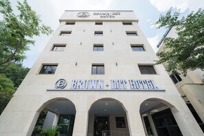 Das äußere Erscheinungsbild des Brown-Dot Hotels mit einem markanten 'B'-Logo, zahlreichen Fenstern und einem Eingang mit Bögen.