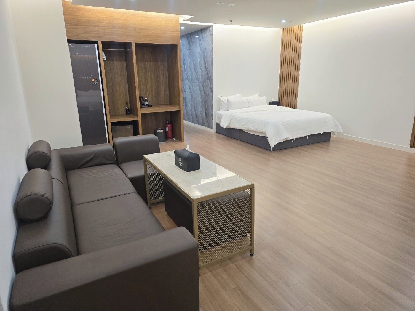 Una habitación de hotel moderna con sofá, una mesita, cama y armario.