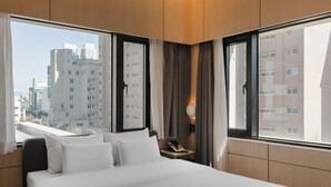 A hotel room with a large bed, a bedside table with a lamp, and a view of tall buildings. - Browndot Hotel Mokpo Gotbawi (Mokpo)