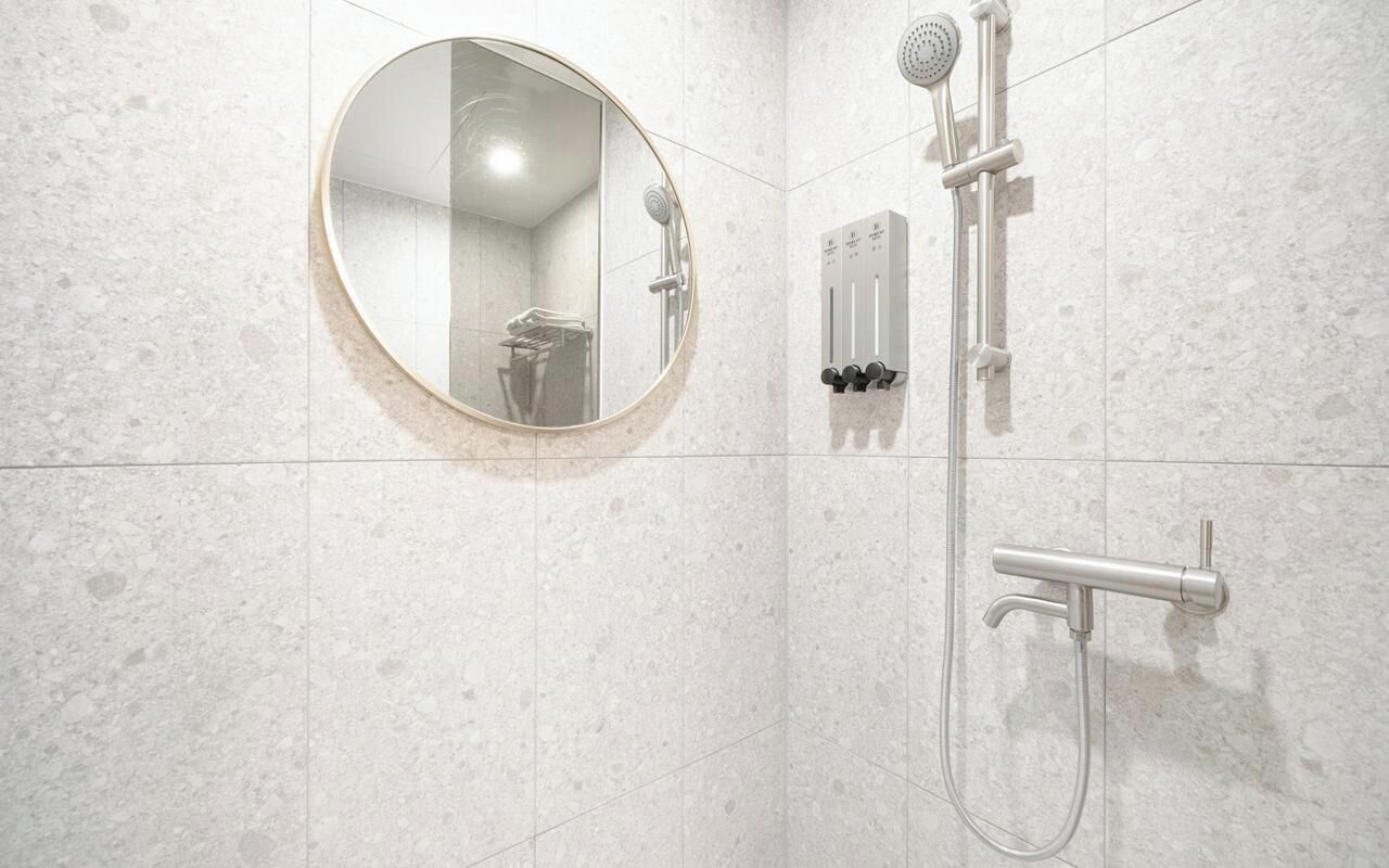 Une salle de bain dotée d’un miroir rond, d’un pommeau de douche à main et d’un panneau de commande fixé au mur.