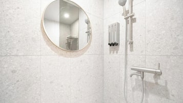 Une salle de bain dotée d’un miroir rond, d’un pommeau de douche à main et d’un panneau de commande fixé au mur.