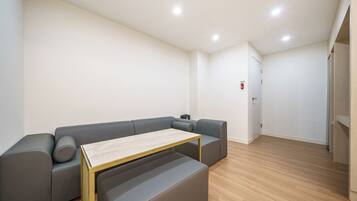 A modern, minimalist room with a grey sectional sofa, a small wooden table, and a door with a fire alarm.