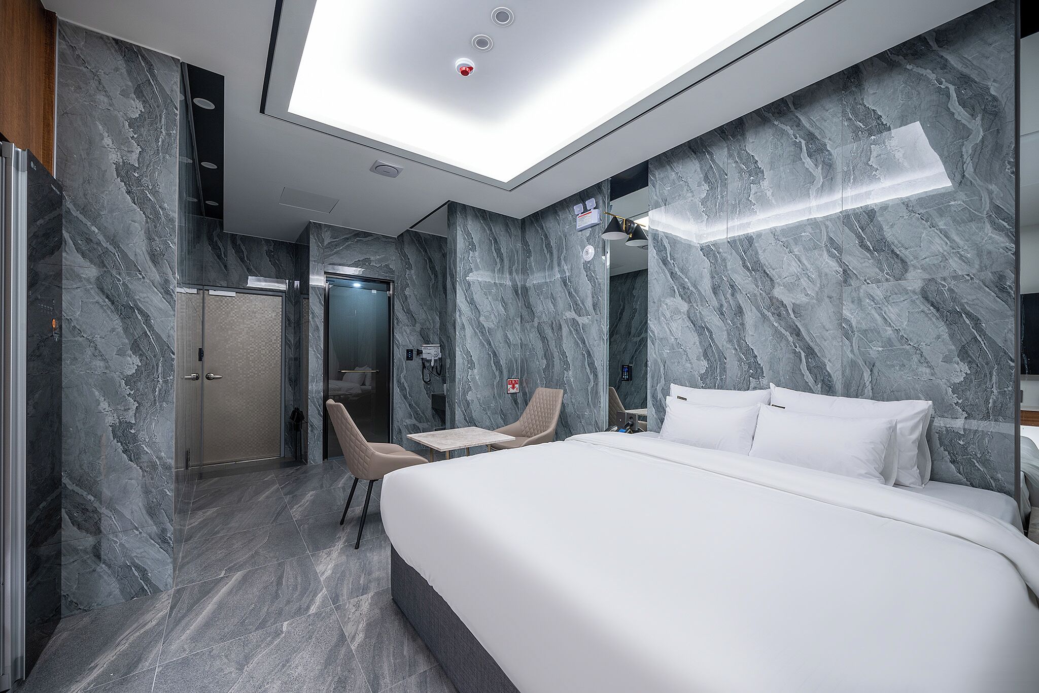 Una habitación de hotel moderna con una cama grande, dos sillas, una mesita y un espejo.