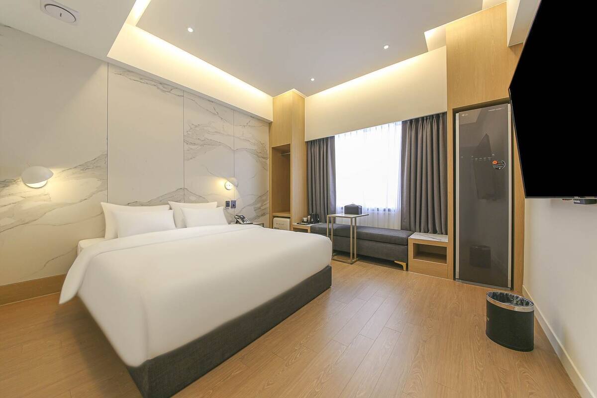 Ein modernes Hotelzimmer mit einem großen Bett, einem Schreibtisch, einem Stuhl und einem Fernseher.