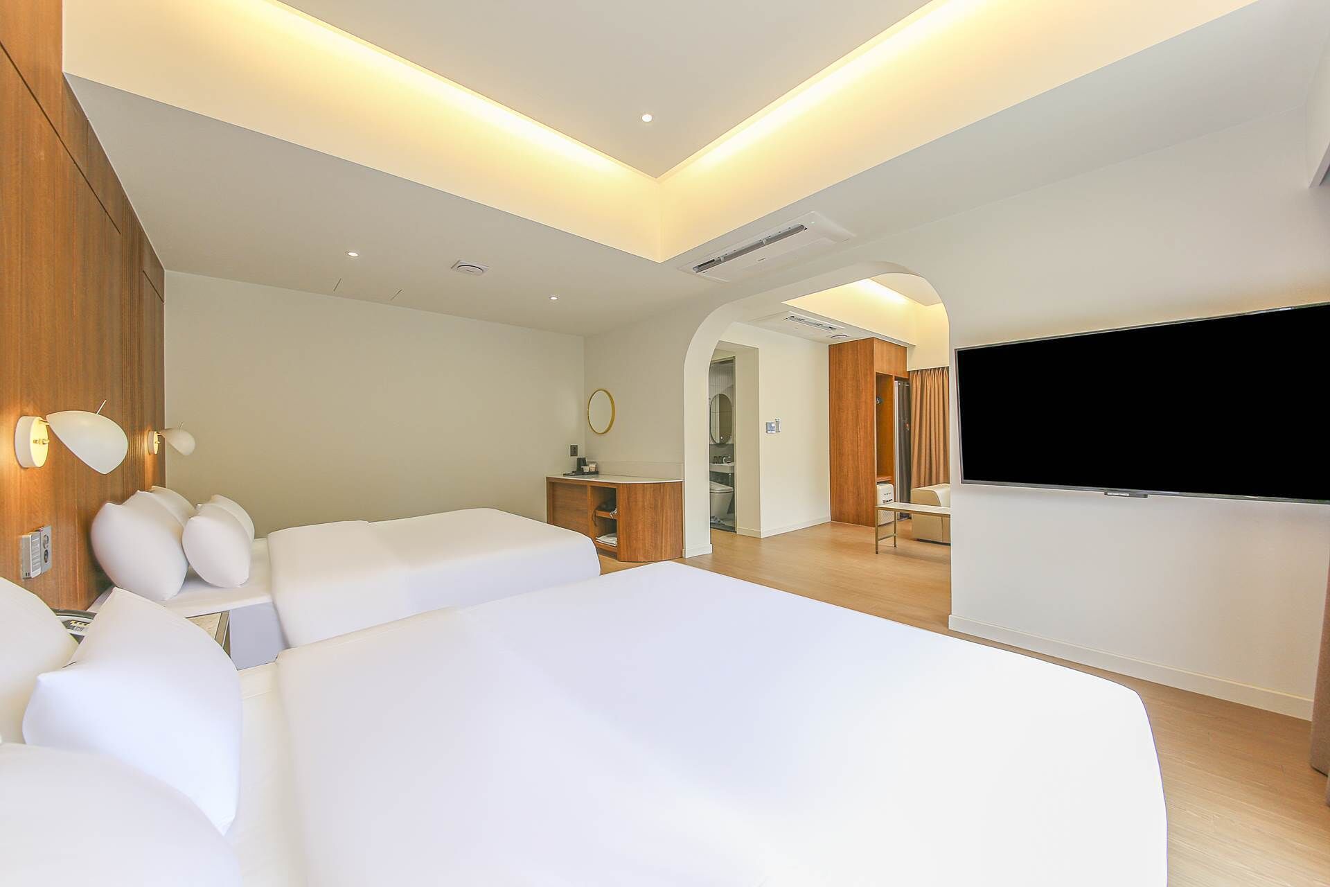 A modern hotel room with two large beds, a TV, a desk, and a walk-in closet.