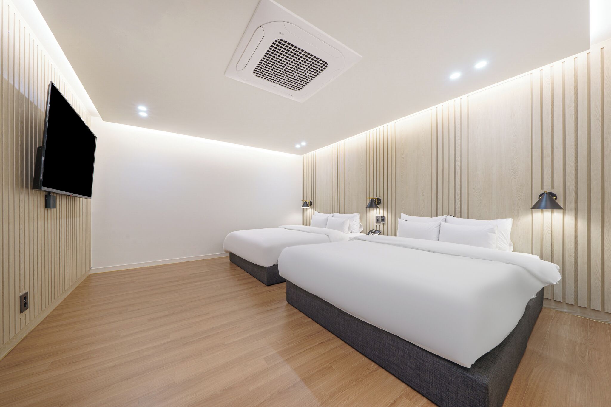 Une chambre d’hôtel moderne, dotée de deux lits, d’un téléviseur à écran plat fixé au mur et d’une bouche d’aération au plafond.