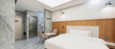 Una camera d'albergo moderna con pavimento in marmo, una testiera in legno, un letto, un'area salotto e una porta in vetro che conduce al bagno.