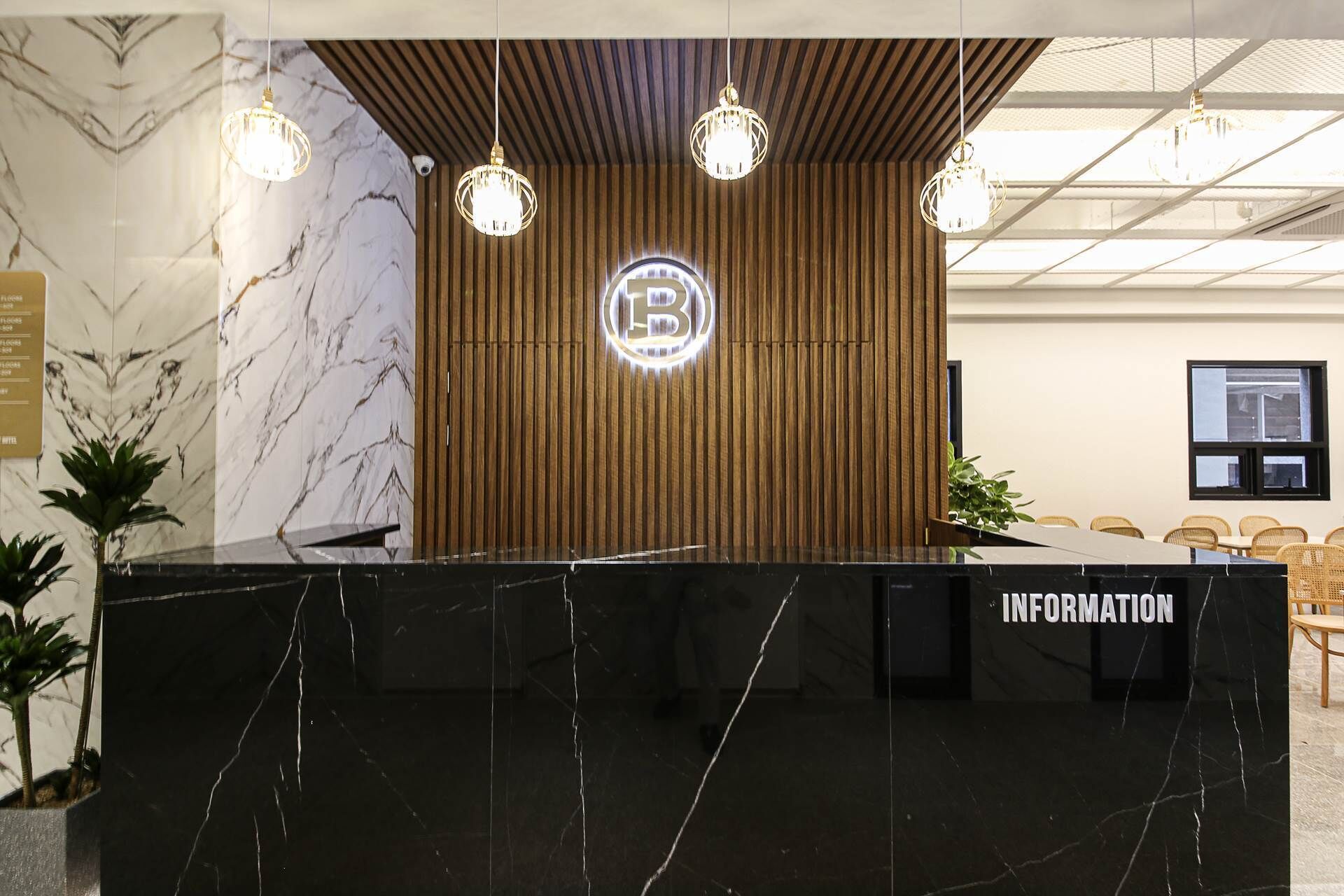 Un mostrador de recepción con encimera de mármol, un panel de pared de madera y un logotipo de 'B' iluminado en el centro.