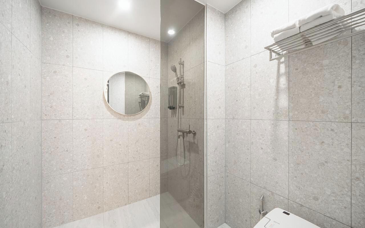 Een moderne badkamer met een douche met glazen wand, een ronde spiegel en een handdoekrek.