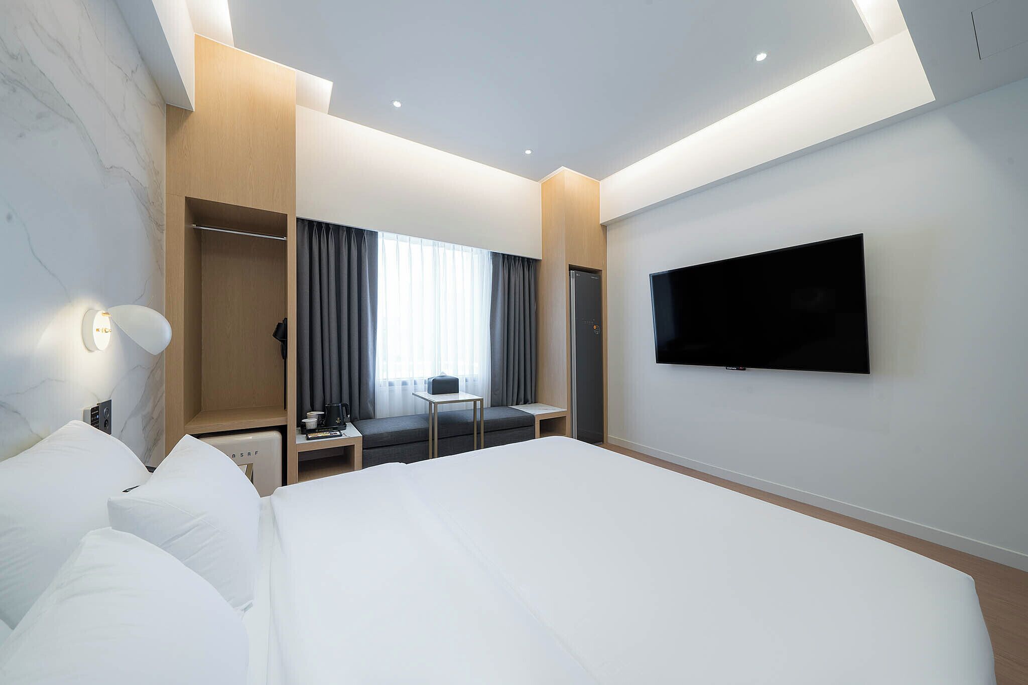 Una habitación de hotel moderna con una cama grande, un televisor de pantalla plana en la pared, una zona de estar con una mesa y sillas, y un armario con espejo.