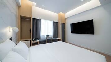 Una habitación de hotel moderna con una cama grande, un televisor de pantalla plana en la pared, una zona de estar con una mesa y sillas, y un armario con espejo.