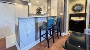 A modern kitchen with a marble island, two bar stools, pendant lighting, and a black refrigerator. - Spacious DC Getaway • Modern Comfort • Walk-In Shower • Near Metro (Washington)