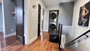 A laundry room with a washer and dryer, a black trash bin, and a staircase with a handrail. - Spacious DC Getaway • Modern Comfort • Walk-In Shower • Near Metro (Washington)