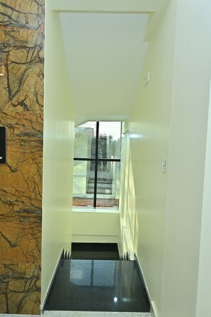 A narrow hallway with a marble wall on one side and a glass door leading to an outdoor area.