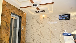 Un hall d’entrée moderne avec des murs en marbre, un ascenseur, un ventilateur de plafond et un téléviseur fixé au mur.