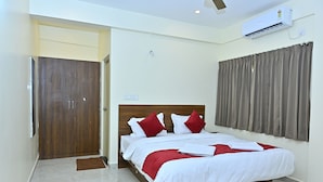 Une chambre d’hôtel avec un lit en bois, une literie blanche et rouge, une porte marron et une fenêtre avec des rideaux.