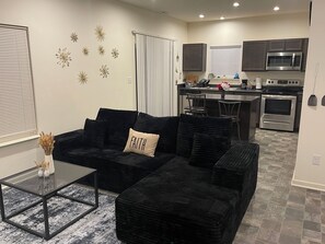 A modern living room with a black sectional sofa, a glass coffee table, and decorative wall art. - 3-bedroom townhome with AC (Indianapolis)