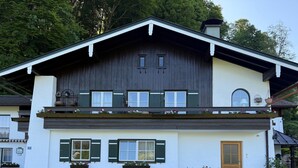 A two-story building with a white facade, dark wooden upper section, and green shutters. - Time out at the mountain spring with 2 bedrooms, bathroom with shower/WC and terrace (Schönau am Königssee)
