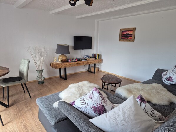 Uma sala de estar moderna com um sofá cinzento, uma mesa de centro de madeira, uma televisão e um quadro na parede.
