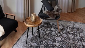 A cozy living room with a black sofa, a wooden side table with a decorative vase, a black chair with a fur throw, and a patterned rug. - Time out at the mountain spring with 2 bedrooms, bathroom with shower/WC and terrace (Schönau am Königssee)