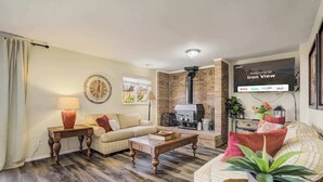 A living room with a sofa, a coffee table, a TV mounted on the wall, and a fireplace. - Iron View! Retreat w/ Hot Tub & Mountain Views (Colorado Springs)