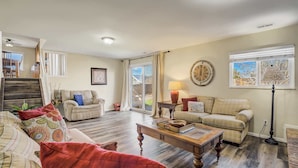 A spacious living room with a wooden coffee table, two sofas, a red armchair, and a large window with curtains. - Iron View! Retreat w/ Hot Tub & Mountain Views (Colorado Springs)