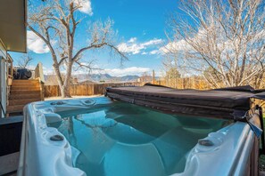 A hot tub with a wooden deck, surrounded by trees and mountains in the background. - Iron View! Retreat w/ Hot Tub & Mountain Views (Colorado Springs)
