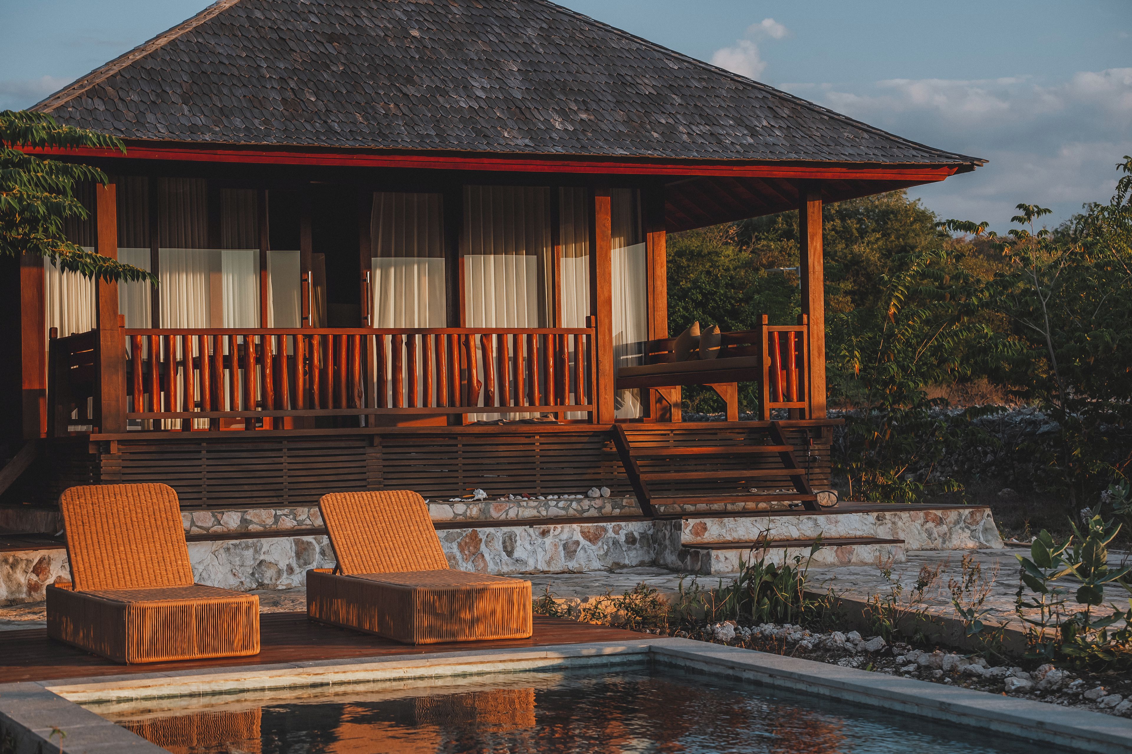 A wooden structure with a balcony, a pool, and wicker furniture.
