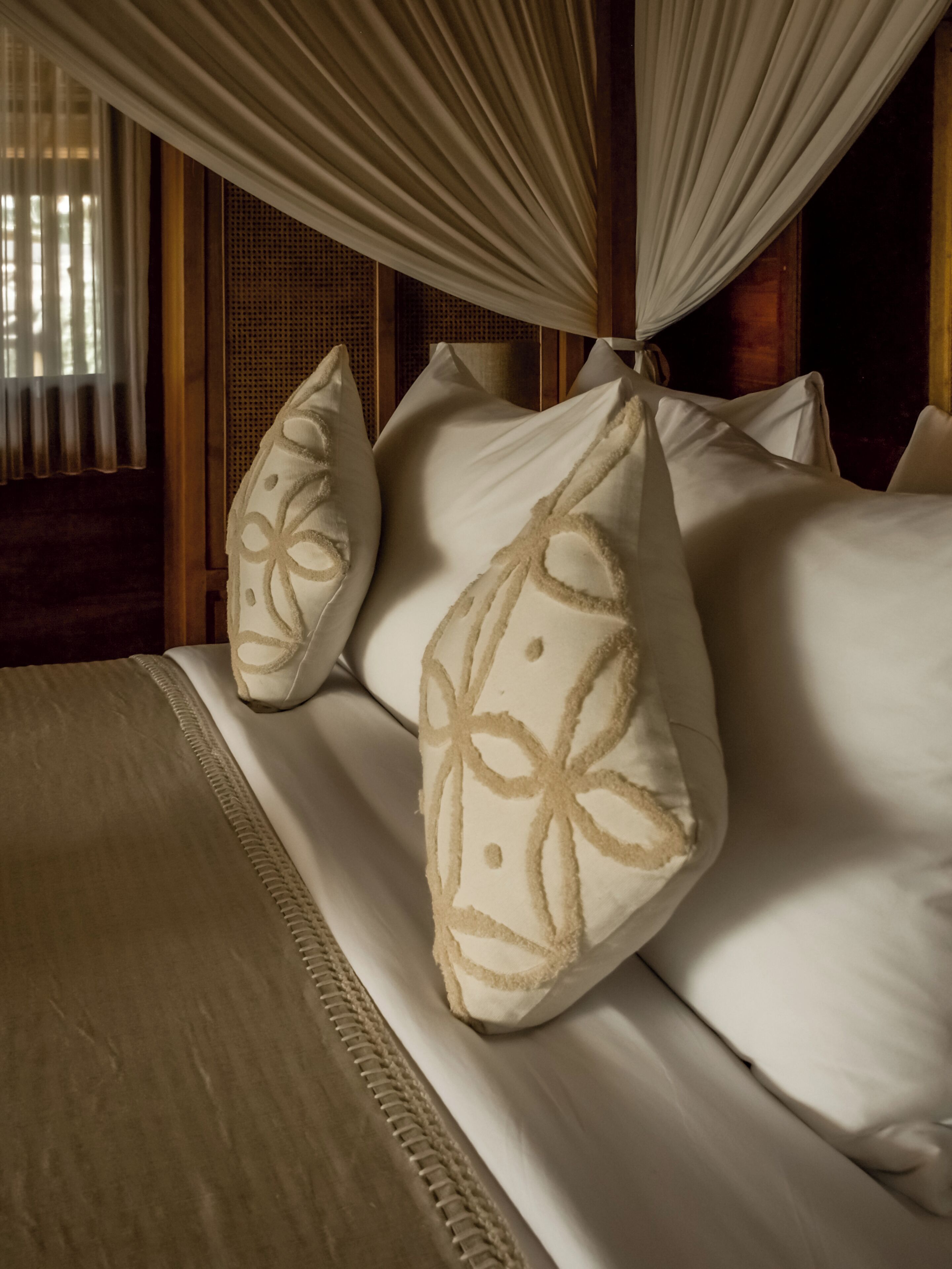 Un lit à baldaquin, un oreiller à motifs et une tête de lit en bois.