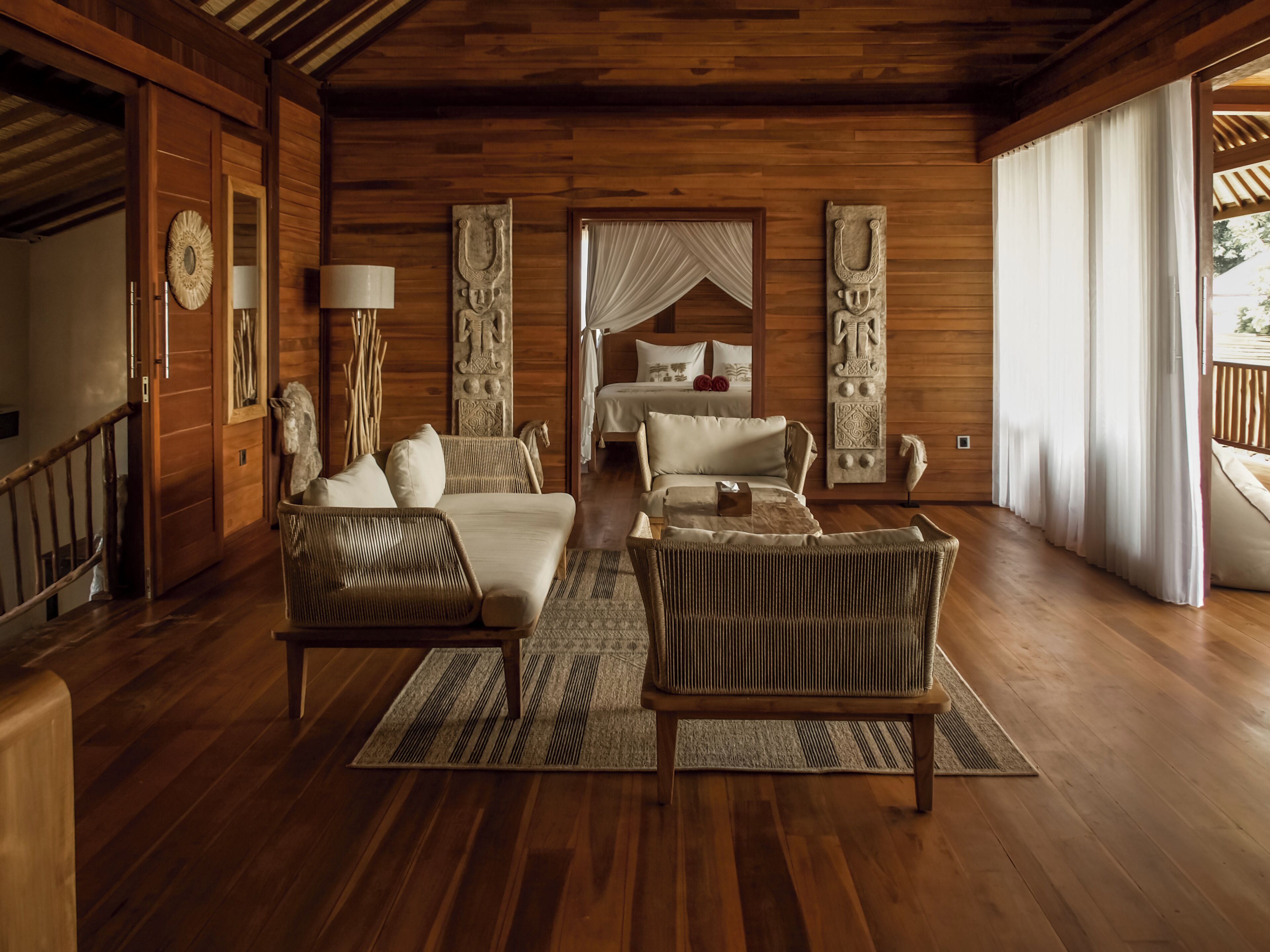A wooden-floored room with a bed, two sofas, a coffee table, and a large window with curtains.