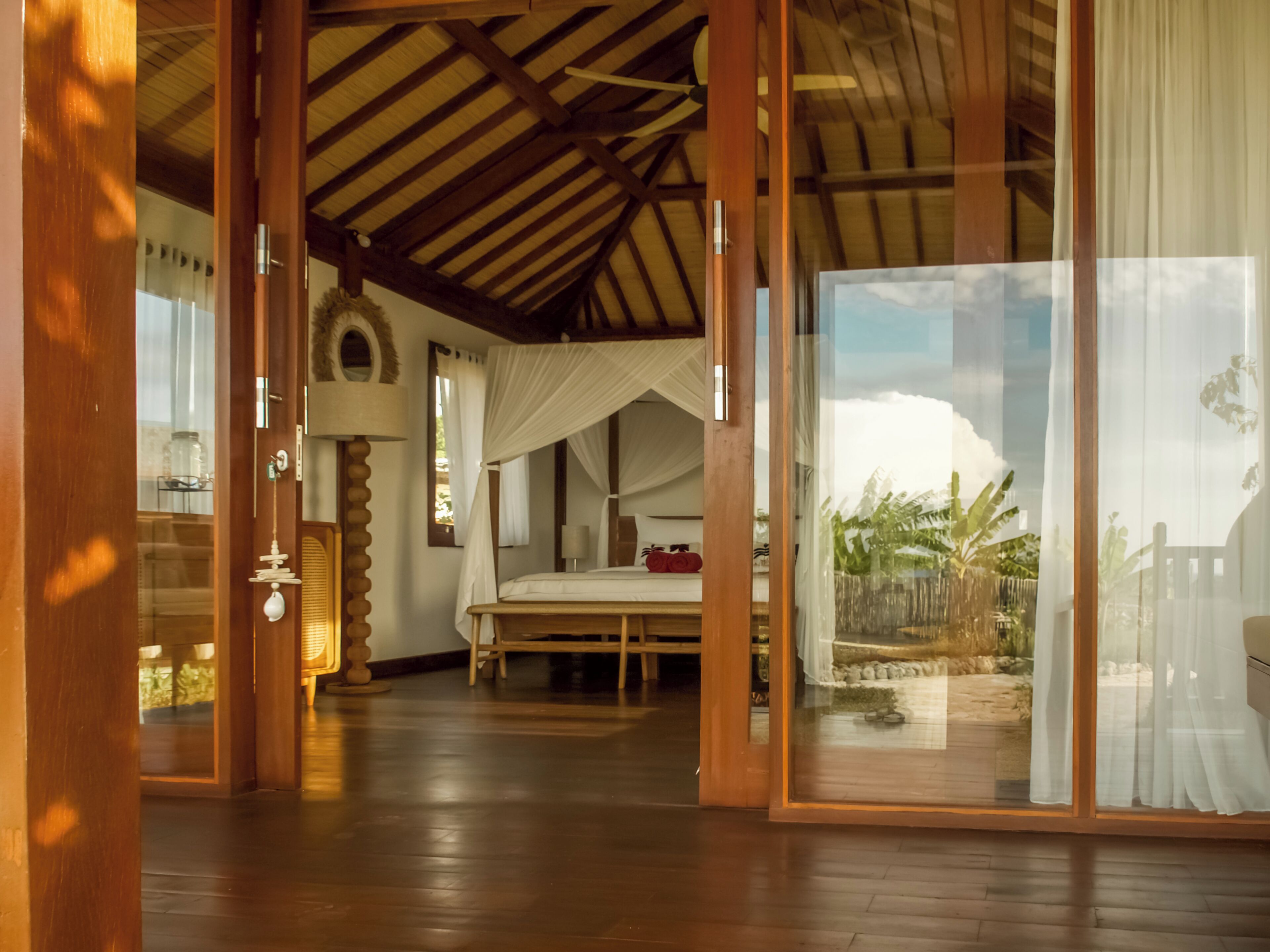 A room with a bed, a canopy, and a view of the outdoors through a glass door.