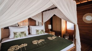 Een bed met hemelbed, kussens met palmboommotieven en een groene deken met bloemversieringen.