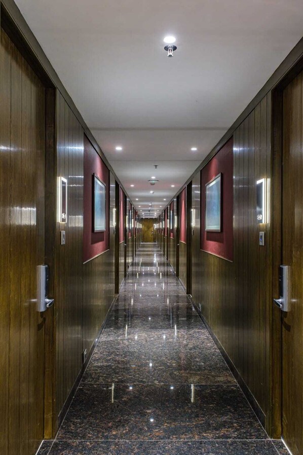 A long, narrow hallway with wooden paneling and red accents, leading to a door at the end. - River Side Suites at Panjim Gymkhana (Panaji)