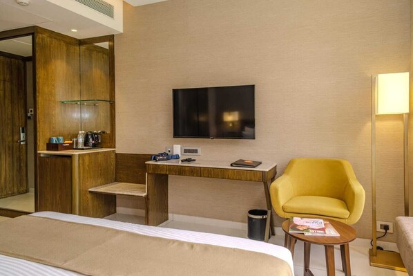 Une chambre d’hôtel avec un lit, un bureau doté d’un téléviseur à écran plat, un fauteuil jaune et une petite table.
