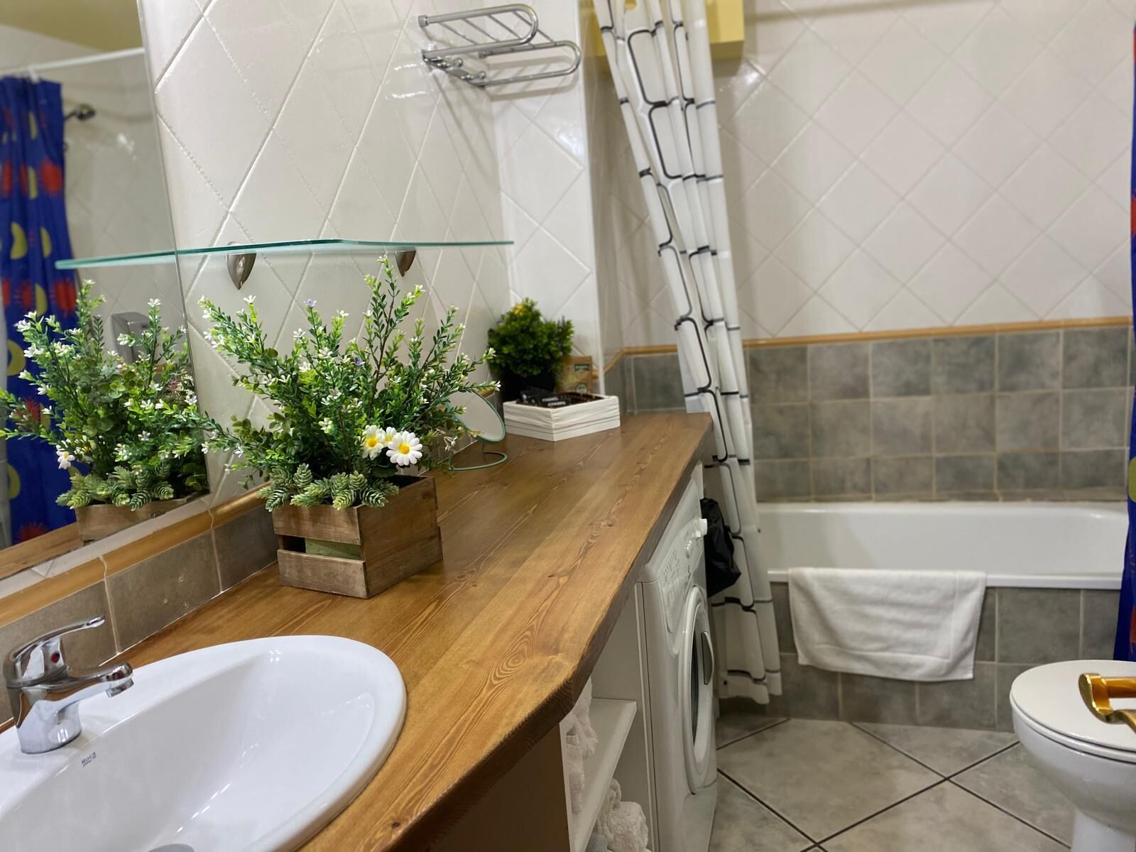 Un baño con encimera de madera, un lavabo blanco, un espejo, zona de ducha e inodoro.