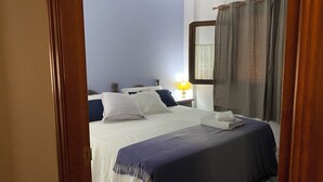 Cama bem arrumada com colcha azul e branca, toalha branca dobrada e abajur.