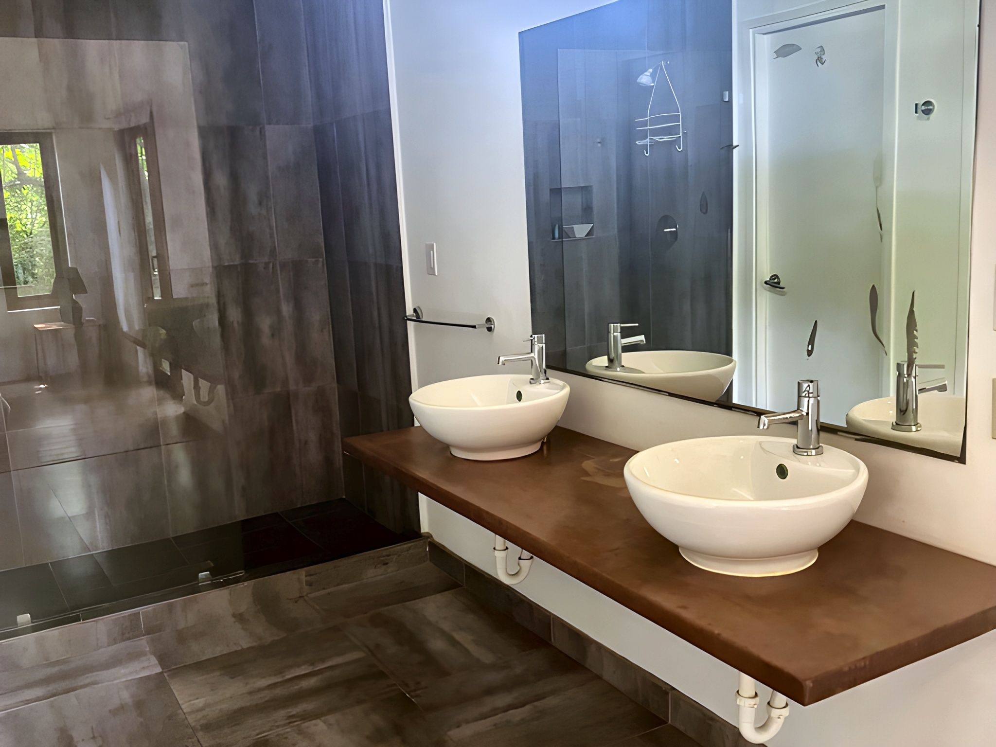 A modern bathroom with two white sinks, a large mirror, and a dark shower area.