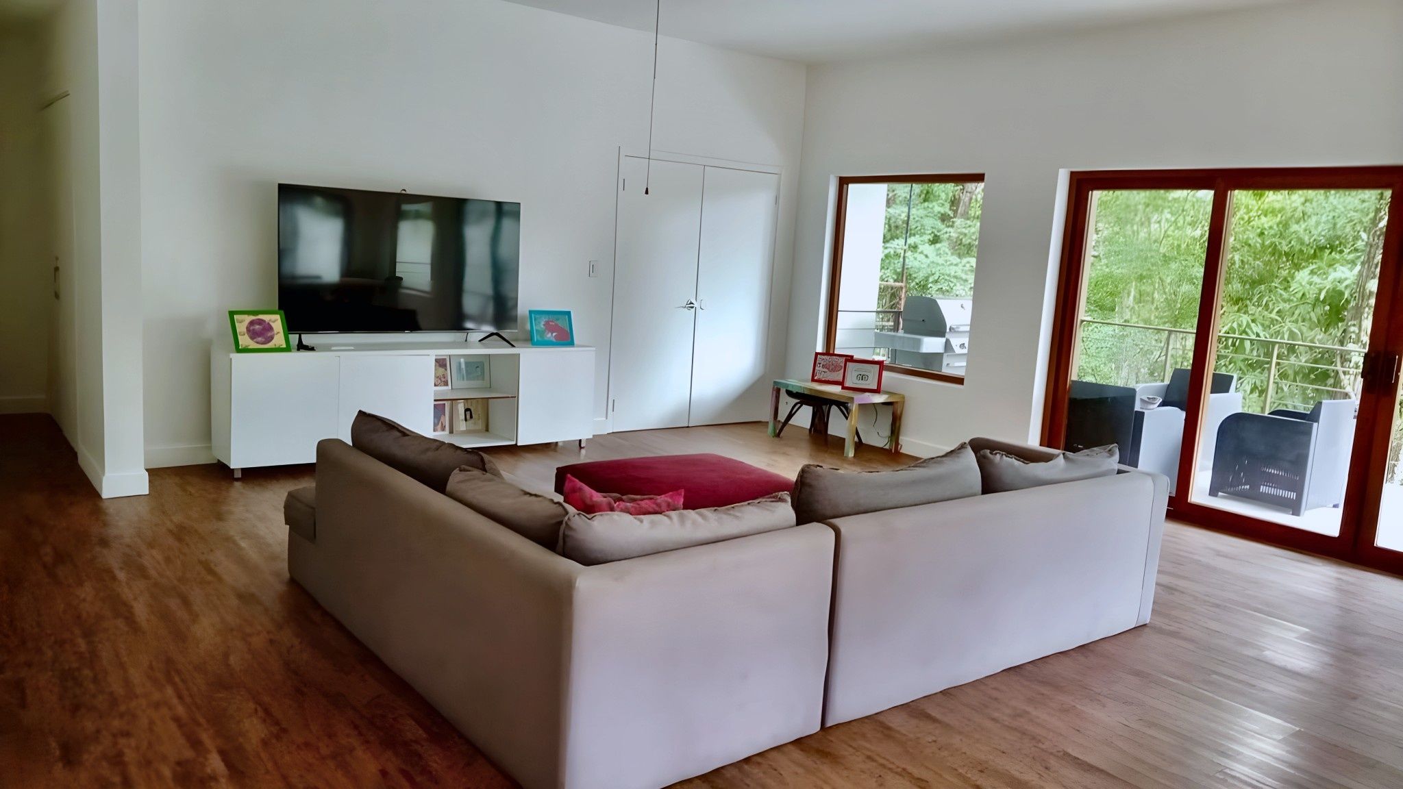 A modern living room with a large sectional sofa, a flat-screen TV, a dining area with a table and chairs, and a sliding glass door leading to an outdoor space.