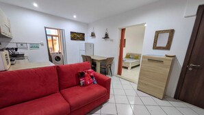 A compact living space with a red sofa, a wooden cabinet, a desk, and a bed. - Valletta Cosy Apartment (Il-Belt Valletta)
