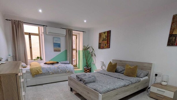 A bedroom with two beds, a desk, a potted plant, and artwork on the walls. - Valletta Cosy Apartment (Il-Belt Valletta)