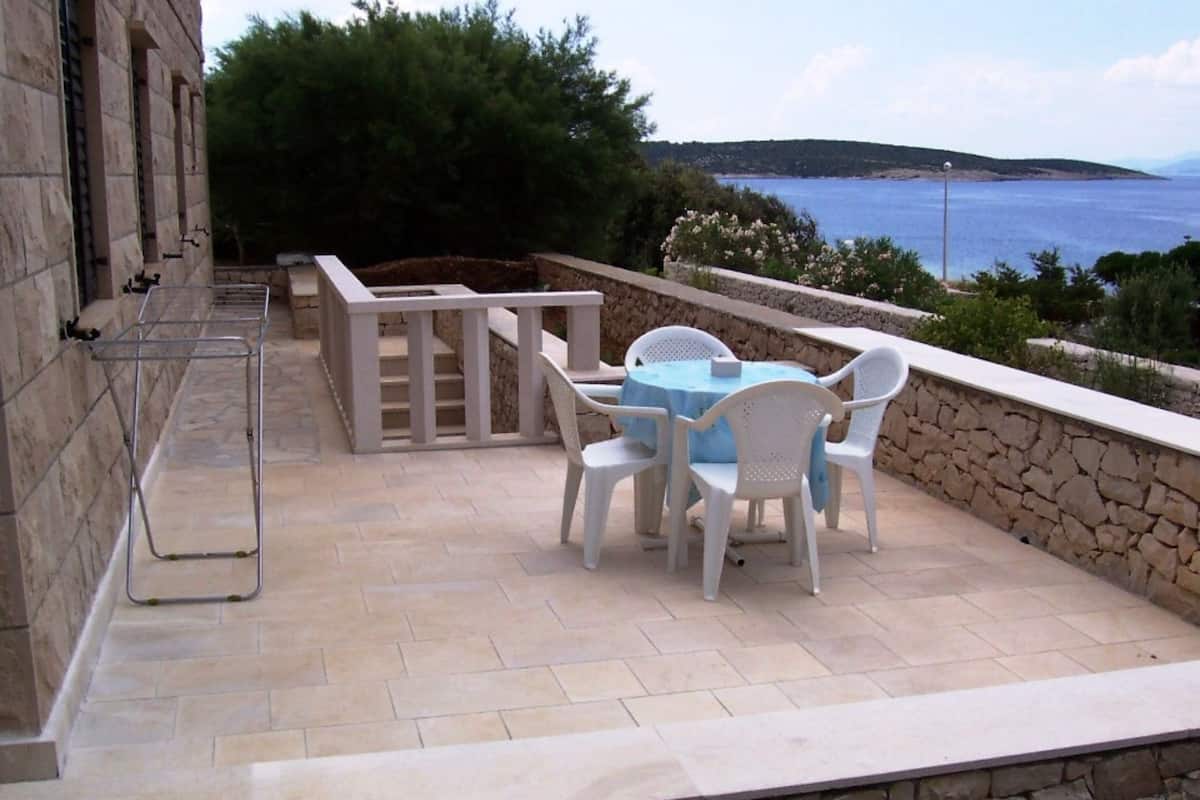 An outdoor patio with a stone wall, a table with chairs, and a view of the sea.