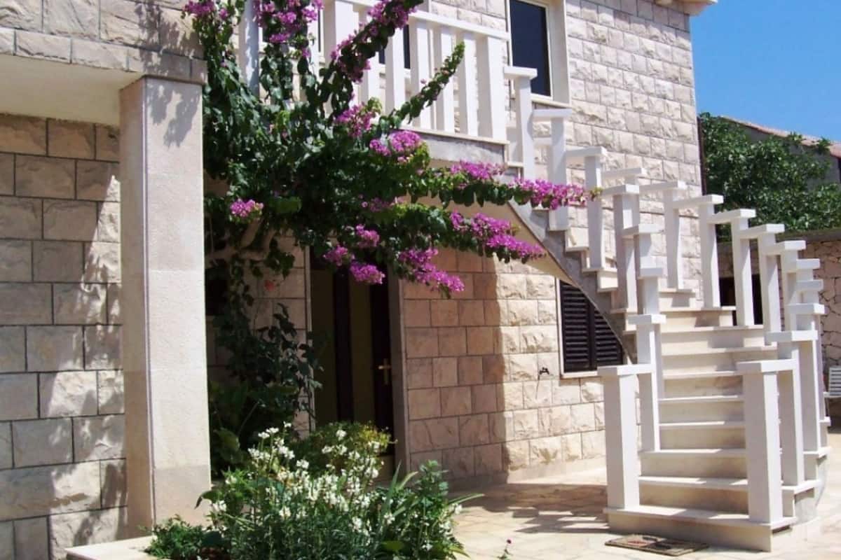 A stone building with a white staircase and a balcony with purple flowers.
