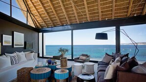 A modern living room with a large window overlooking the sea, furnished with sofas, a coffee table, and decorative items.