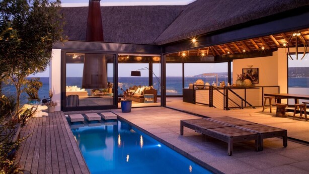A modern outdoor pool area with a glass enclosure, seating, and a view of the sea.