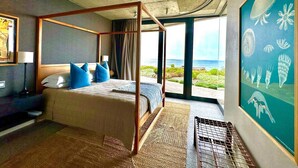 A four-poster bed with blue pillows, a television, and a view of the ocean.